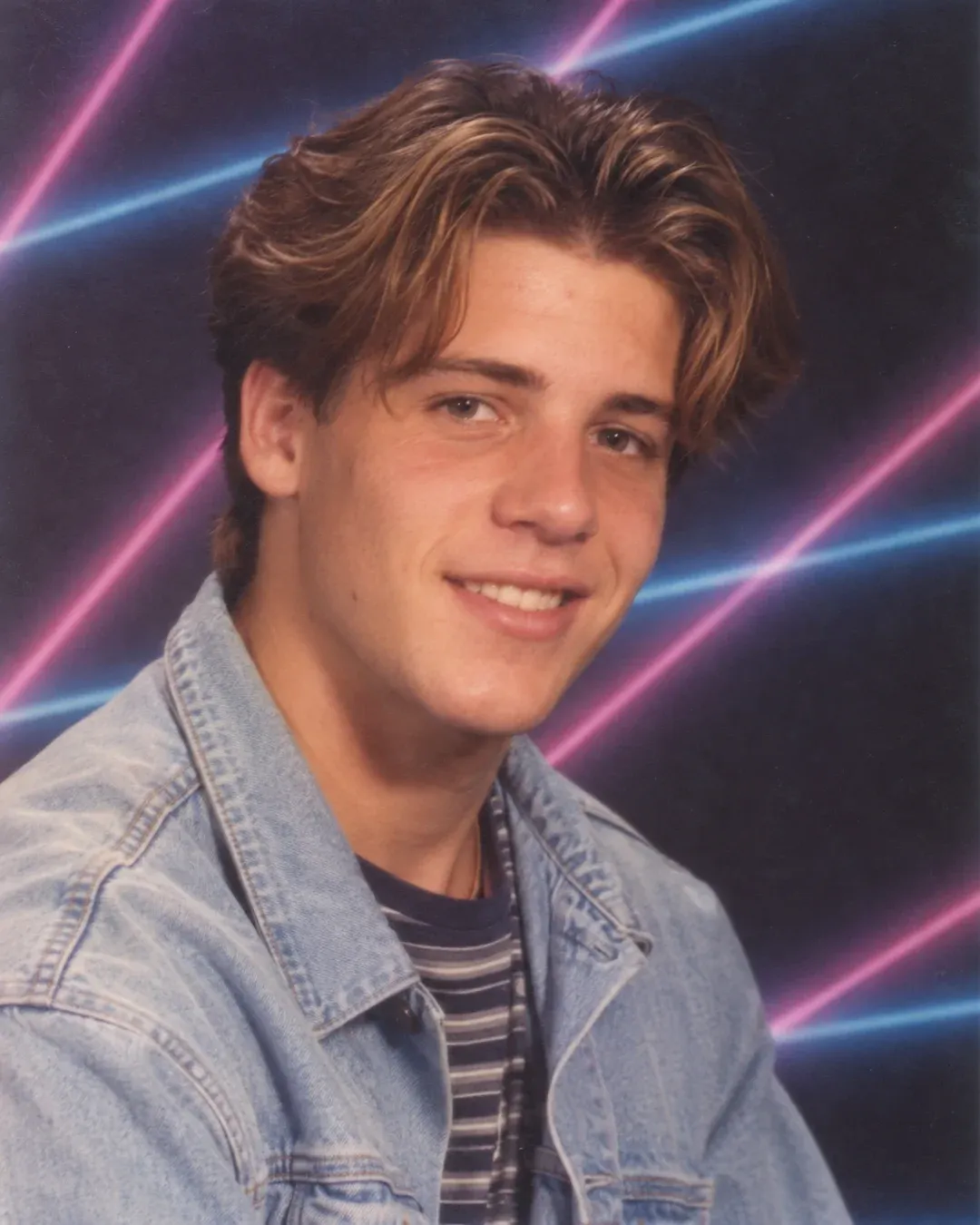 Example result: A 1990s-style school yearbook portrait of a smiling person in a denim jacket in front of a blue laser backdrop.
